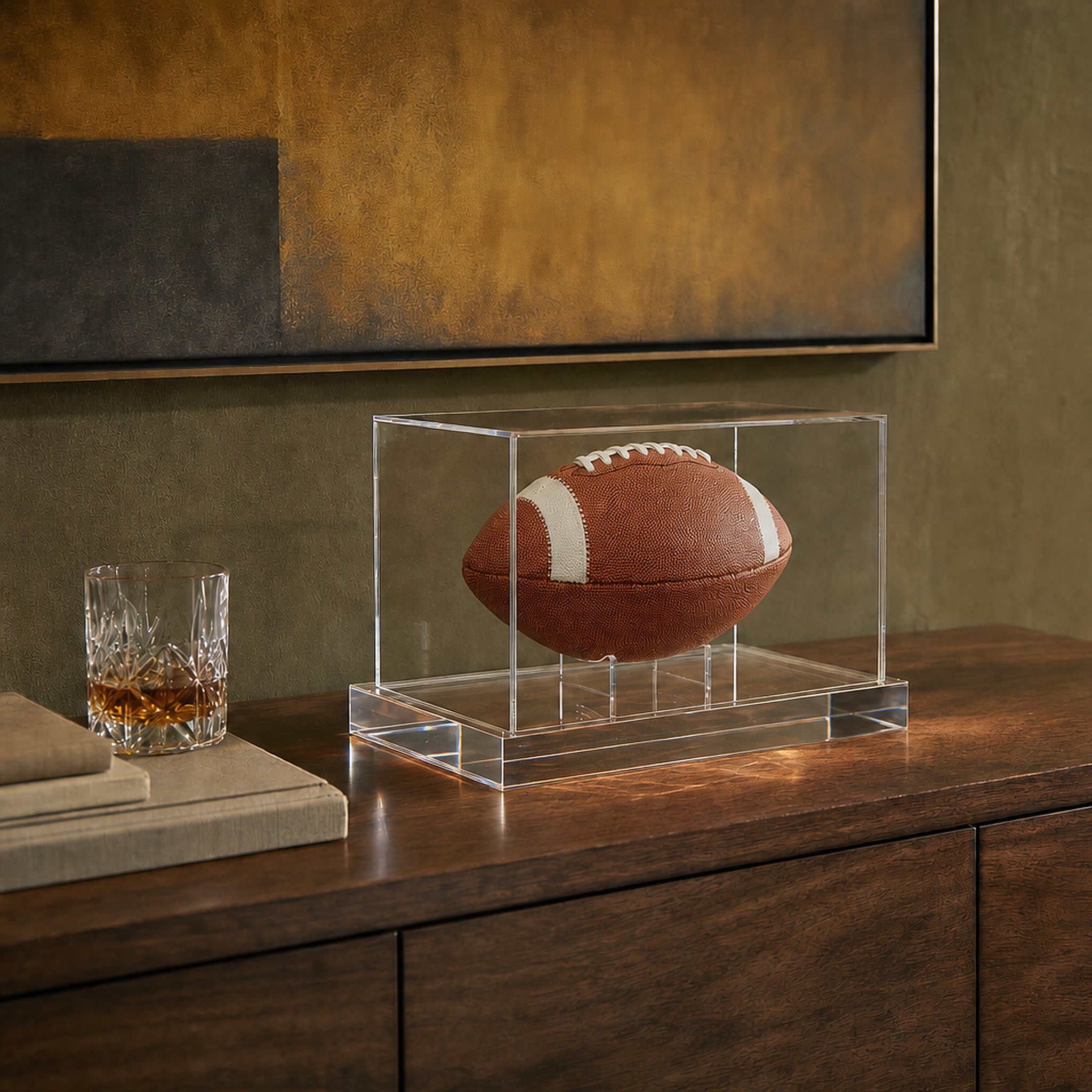 Wexel Art luxe football display case with 98% UV acrylic cover styled on a walnut credenza in a high-end residential game room with olive plaster walls, abstract art and a felt card table